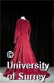 The dress is lined with a heavy cotton and the outer material is thick deep red velvet.
It has a v-neck and darts down the front to give a fitted effect. There are hook and eye fastenings from the back of the neck to the lower waist. It has long sleeves that have two popper fastenings on the inside cuff and meet at a point over the top of the hand. It has a very full floor length skirt.