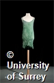 One dress (820mm in length) is green/blue and made of a silk like shiny fabric. It has thin straps, is sleeveless with a scooped back. The material is crinkled.
The other twenty dresses are made from muslin/cotton and have been tie died using various shades of blue and green. (One 'dress' is the same material as the others and has been sewn at one edge but is just a piece of fabric, perhaps a dress that was started but unfinished). Nine dresses have silk linings in. The dresses have bateau style necklines, some are sleeveless but cover the shoulder, and others have thin straps. They are all crinkled. Some have sewn hems and others do not, the hemlines look uneven on all the dresses. Fifteen dresses are twisted, presumably to keep the crinkled effect; the others are untwisted and have been packaged as such.
