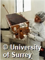 Photograph of a student or member of staff examining a microsatellite in a laboratory of the Surrey Satellite Technology Ltd at the University of Surrey
